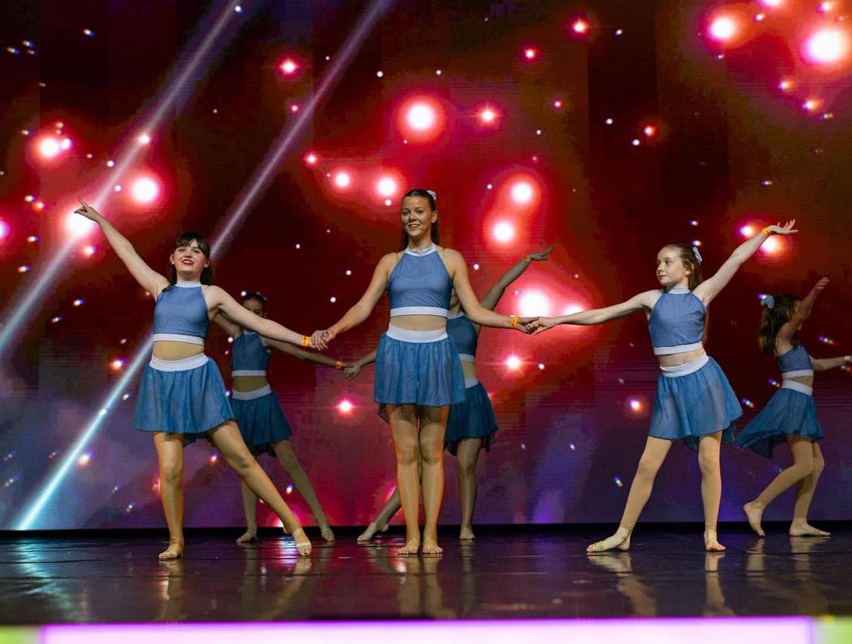 Dancers in blue performing a modern routine on stage under red lights