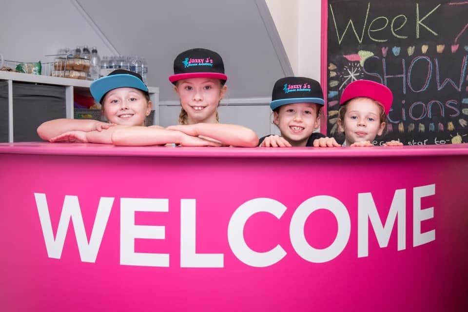 Children peeking over the pink Welcome desk